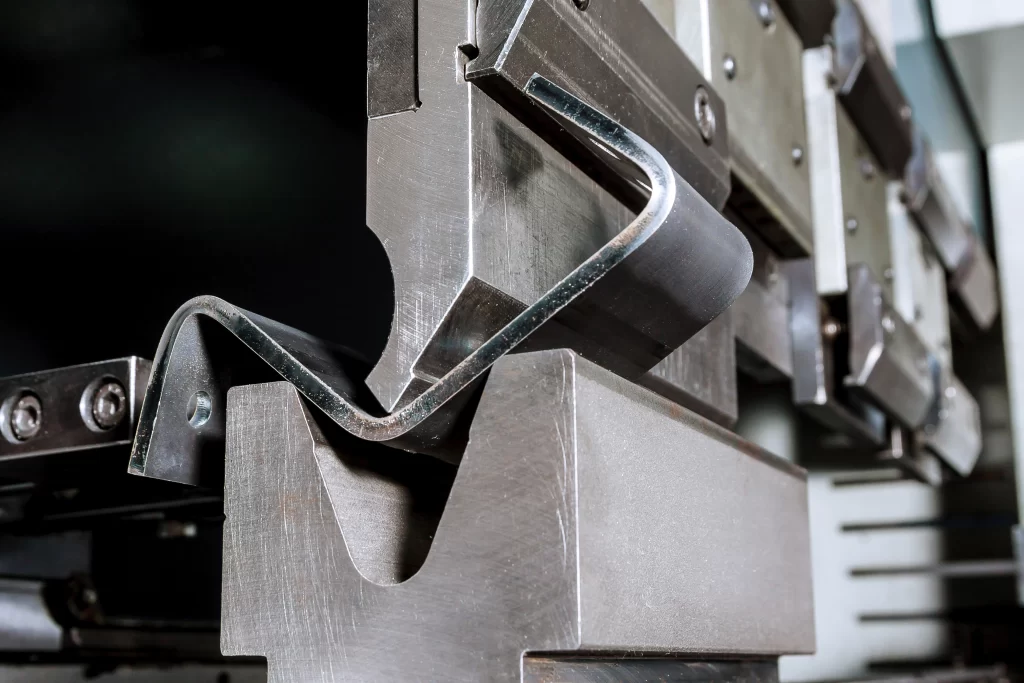  Close-up de uma prensa dobradeira industrial em operação, conformando com precisão uma chapa de metal para um serviço de estamparia metálica.
